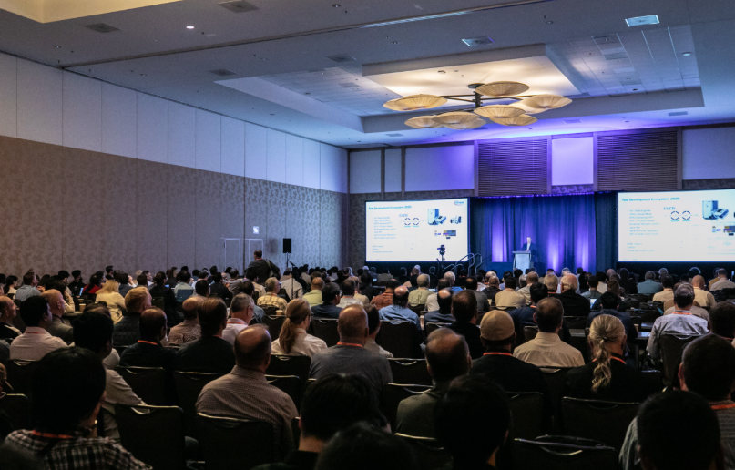 A full conference session at ITC 2026, with the speaker at the podium and slides on two screens.